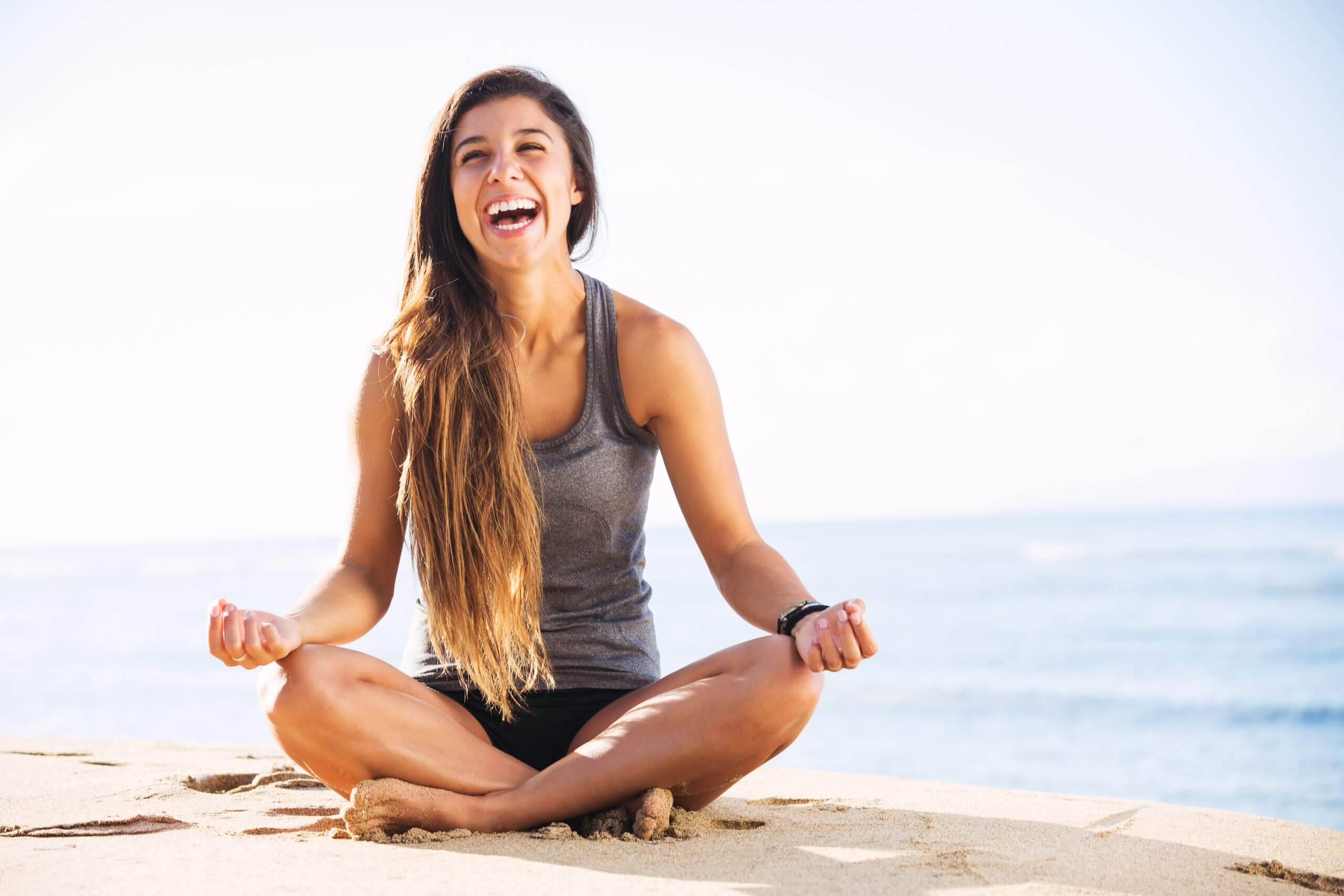Laughing woman sitting on the beach to meditate and restore energy balance.